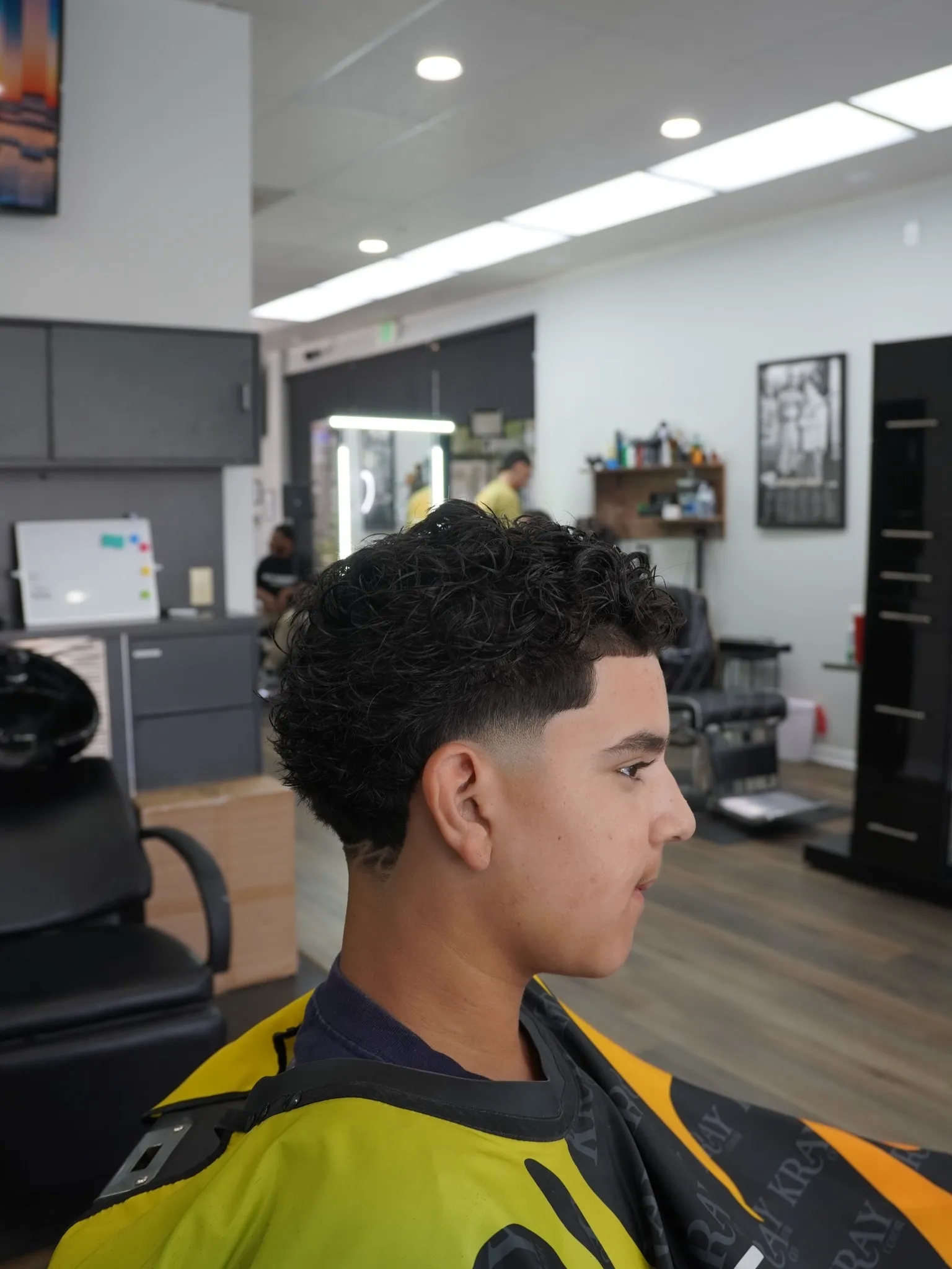 Boy with a fresh taper fade sitting in the chair, the shop behind him
